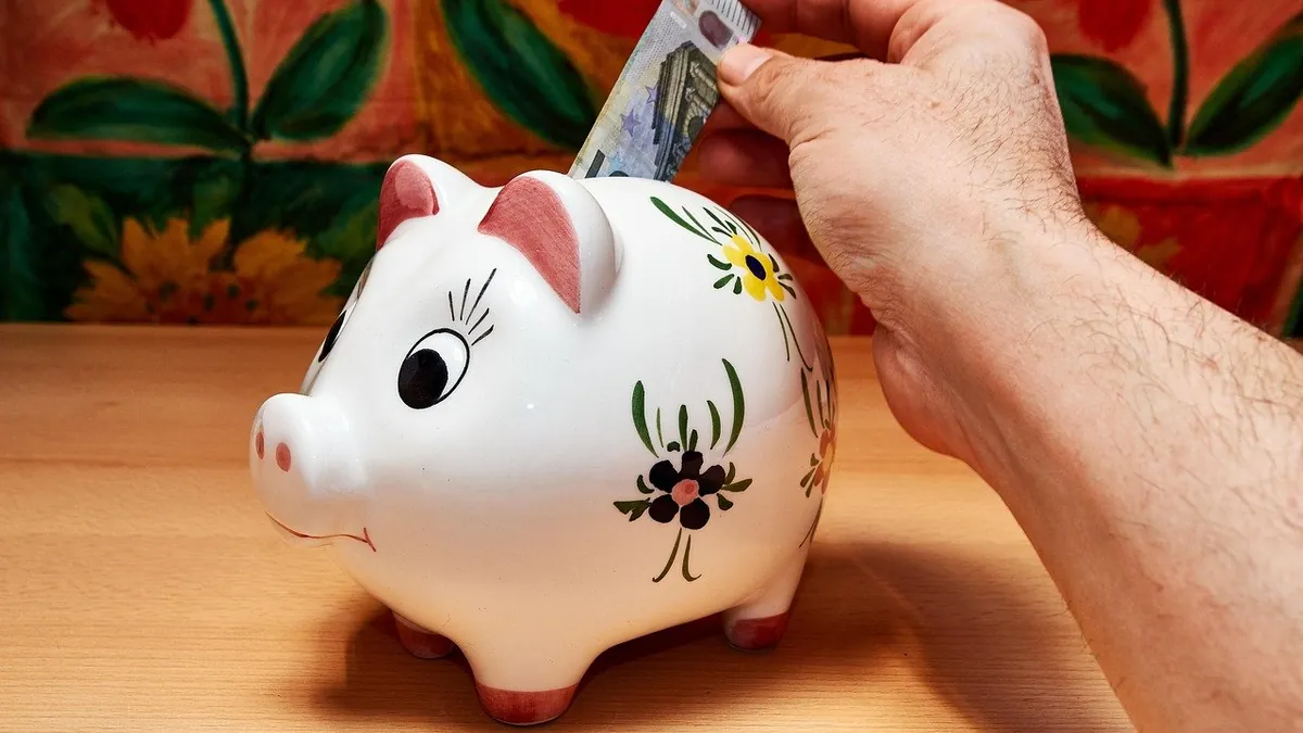 Χέρι βάζει χαρτονόμισμα σε πορσελάνινο κουμπαρά