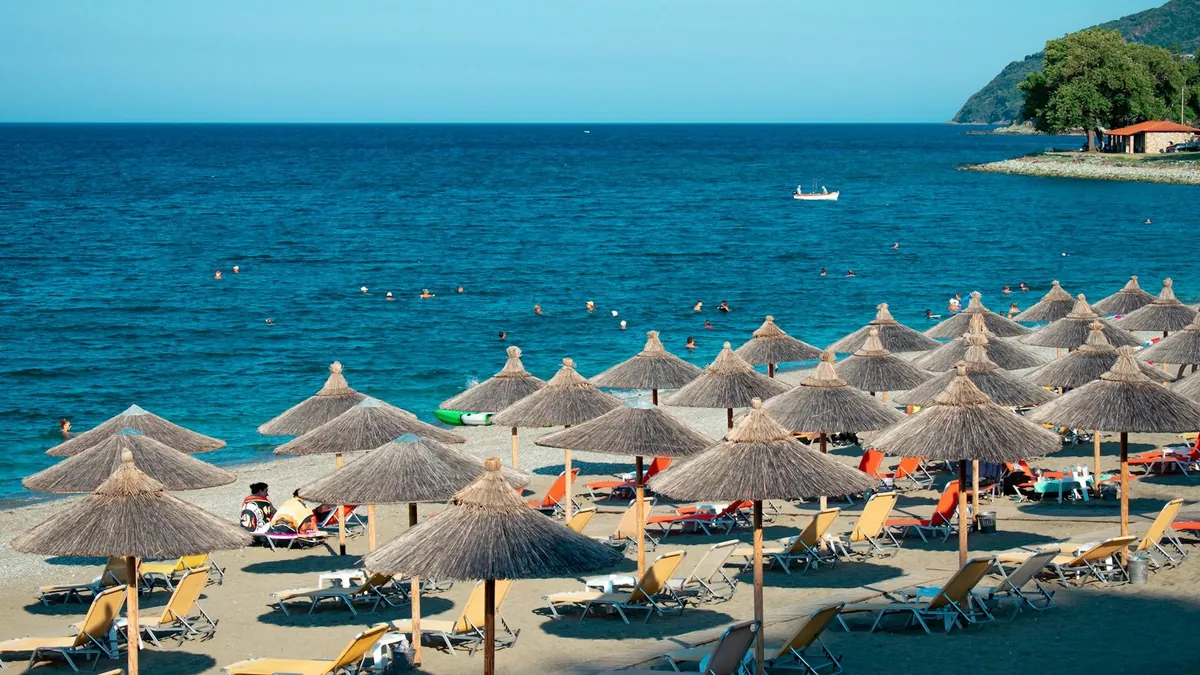 Παραλία με ψάθινες ομπρέλες και ξαπλώστρες δίπλα σε γαλάζια θάλασσα